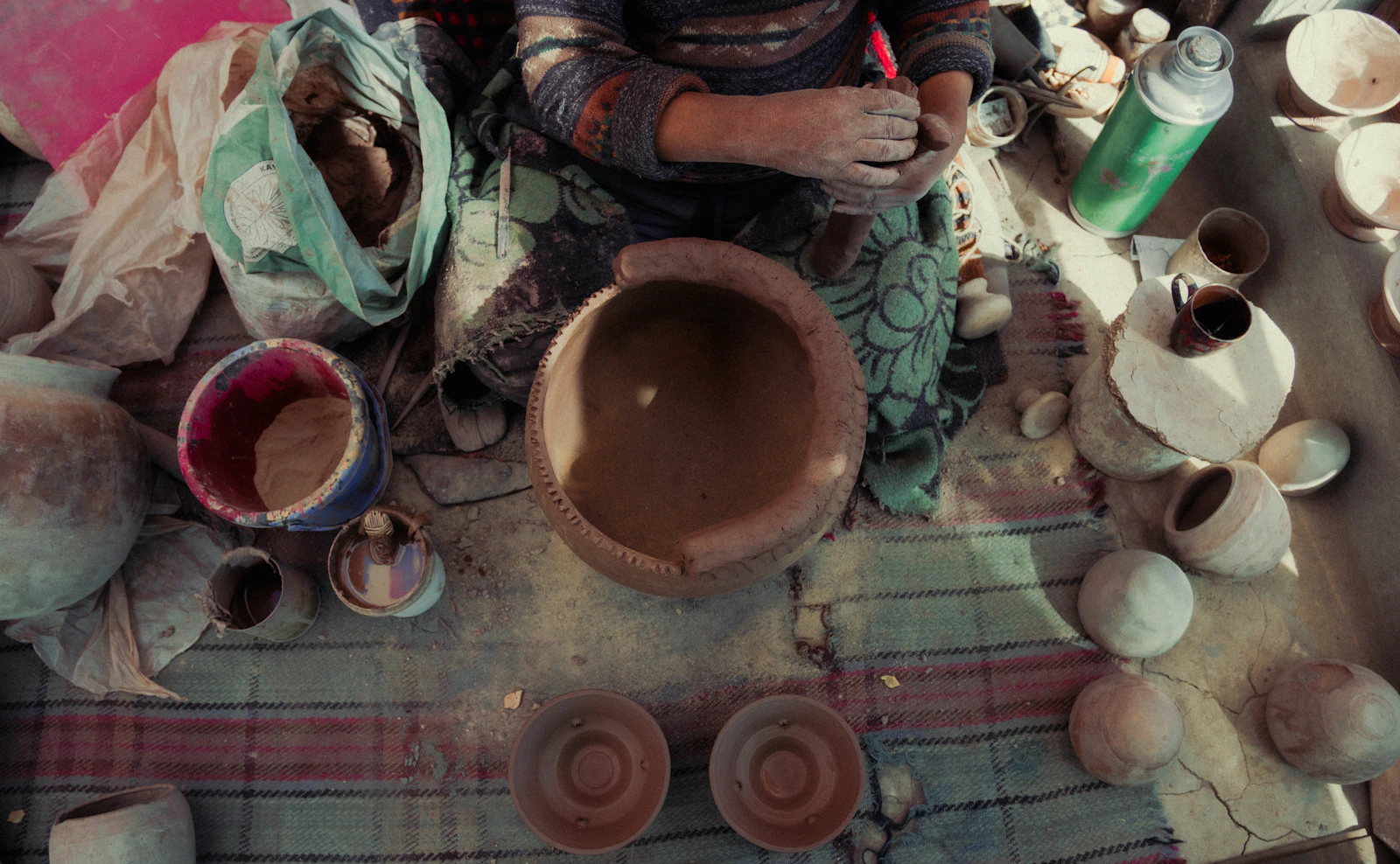 An artisan shaping clay surrounded by handmade pottery